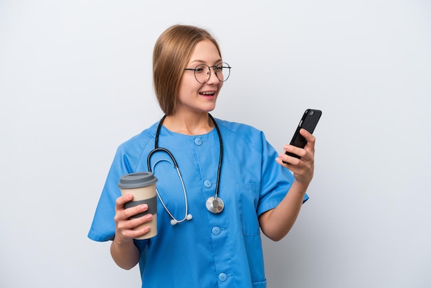 Joven enfermera doctora aislada de fondo blanco sosteniendo café para llevar y un móvil