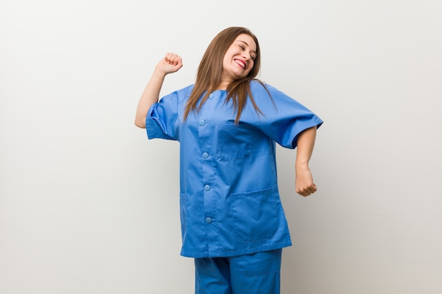 Joven enfermera mujer contra una pared blanca bailando y divirtiéndose.
