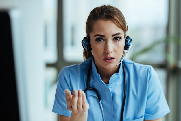 Joven enfermera seria con auriculares y asesorando a un paciente mientras trabaja en un centro de llamadas médicas