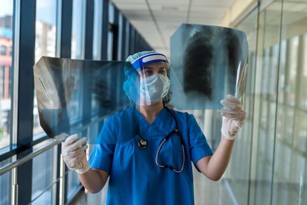 Joven enfermera con traje protector y careta comprobando la imagen de la radiografía de tórax, covid19. Pandemia