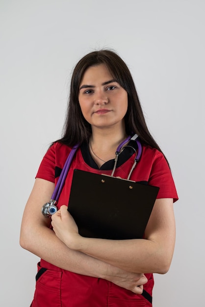 Joven enfermera vistiendo uniforme rojo con estetoscopio mantenga portapapeles aislado sobre fondo blanco Concepto médico