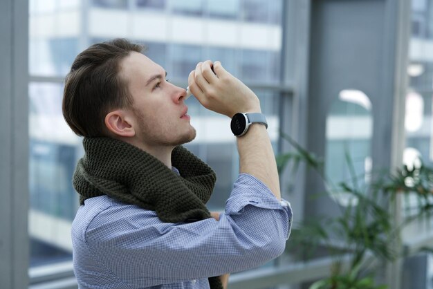 Un joven enfermo gotea inyectando una gota nasal para la nariz tapada y la secreción nasal