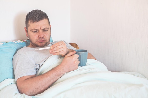 Foto joven enfermo con un termómetro en la cama de la casa