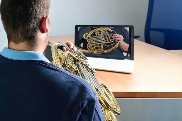 Joven ensaya una lección de música con un trombón en una computadora portátil