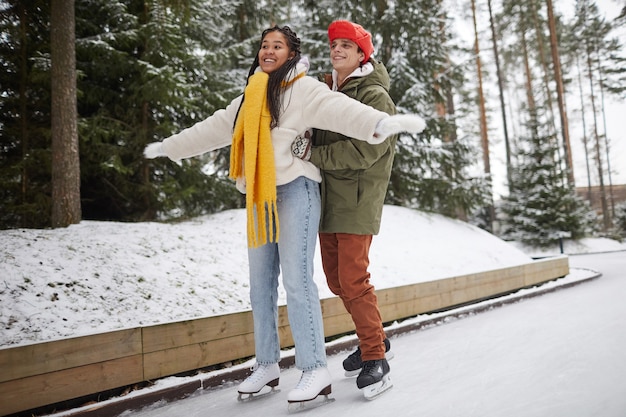 Joven enseñando a su novia a patinar durante su tiempo en la pista de patinaje en el parque