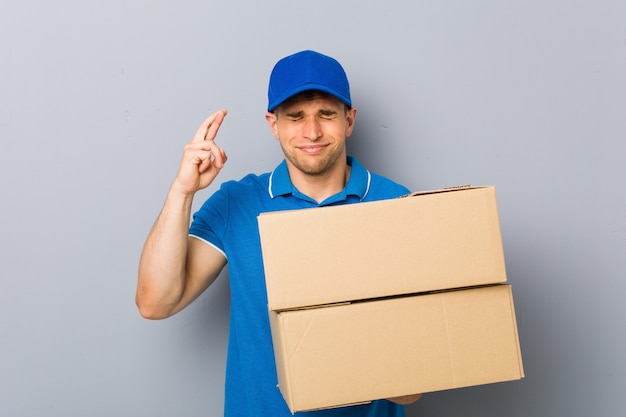 Joven entregando paquetes cruzando los dedos para tener suerte