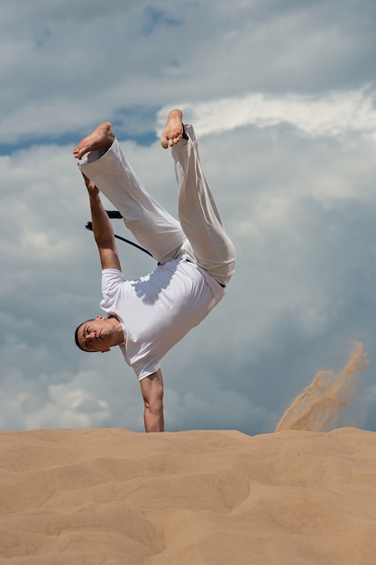 Un joven entrena a capoeira contra el cielo. Un hombre realiza un truco acrobático.