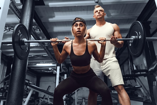 Un joven entrenador personal masculino ayuda a una mujer a estimular los músculos mientras hace sentadillas fitness m