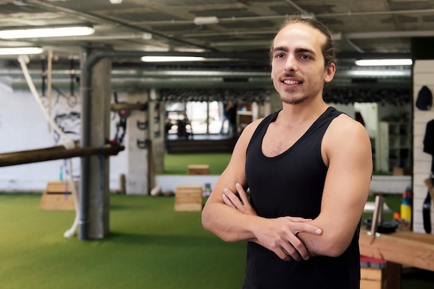 Joven entrenador posa con los brazos cruzados en su gimnasio