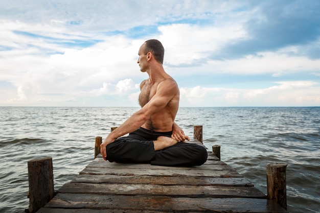 Joven entrenador de yoga practicando ejercicios de yoga en un muelle de madera a orillas del mar o del río