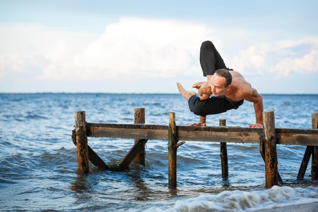 Joven entrenador de yoga practicando ejercicios de yoga en un muelle de madera a orillas del mar o del río