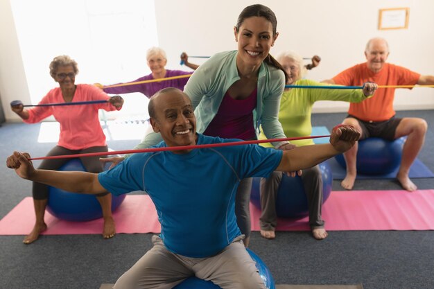 Joven entrenadora ayudando a un anciano en el estudio de fitness