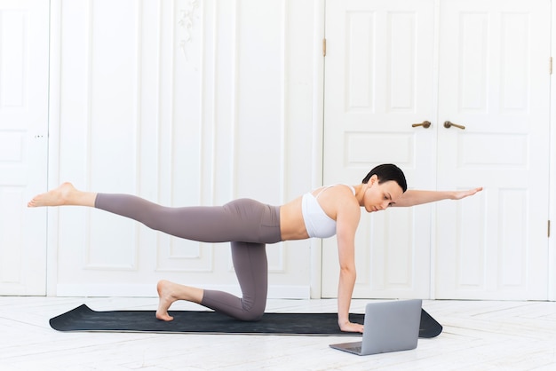 Una joven entrenadora enseña yoga de forma remota a través de Internet con su computadora portátil