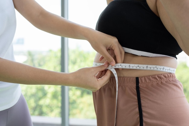 Foto una joven entrenadora mide la capa de grasa de una mujer con sobrepeso y cintura en un gimnasio
