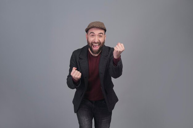 Joven entusiasta con chaqueta y gorra con los brazos arriba en una foto de estudio