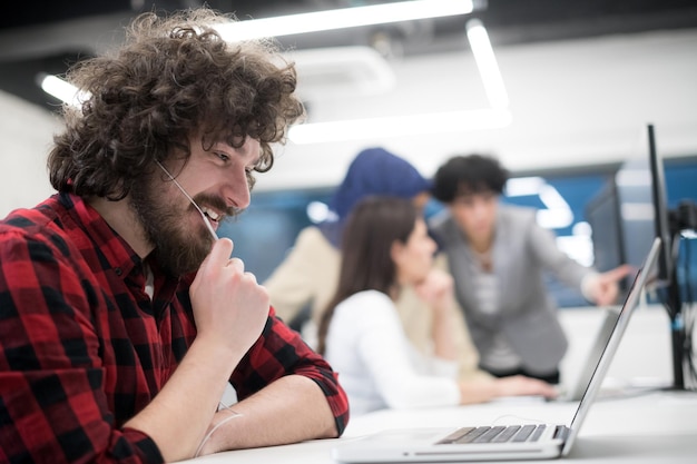 Joven equipo empresarial multiétnico de desarrolladores de software que trabajan juntos usando una computadora portátil y de escritorio mientras escriben código de programación en la oficina de inicio moderna