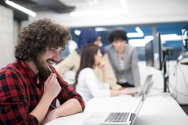 Joven equipo empresarial multiétnico de desarrolladores de software que trabajan juntos usando una computadora portátil y de escritorio mientras escriben código de programación en la oficina de inicio moderna