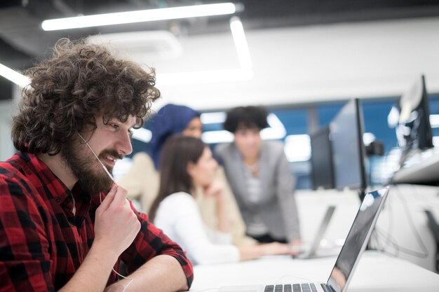 Joven equipo empresarial multiétnico de desarrolladores de software que trabajan juntos usando una computadora portátil y de escritorio mientras escriben código de programación en la oficina de inicio moderna