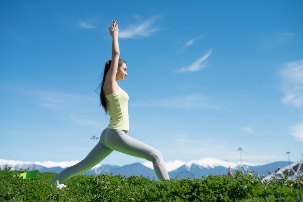 Una joven esbelta haciendo yoga sobre hierba verde en el parque meditando