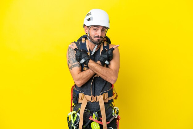 Foto joven escalador caucásico aislado de fondo amarillo apuntando a los laterales con dudas