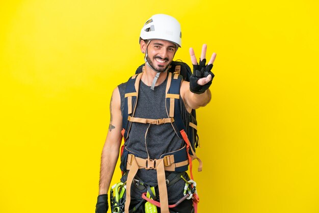 Joven escalador caucásico aislado de fondo amarillo feliz y contando tres con los dedos