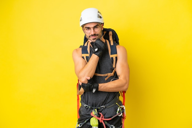 Joven escalador caucásico aislado de fondo amarillo con gafas y sonriendo