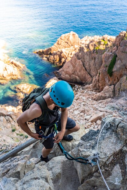 Joven escalador fuerte éxito caminando sobre rocas sobre el mar con cuerda y casco