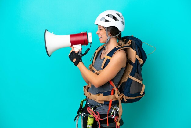 Una joven escaladora italiana aislada de fondo azul gritando a través de un megáfono