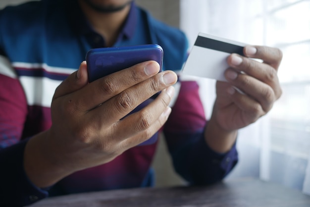 Joven escribiendo detalle de tarjeta de crédito en teléfonos inteligentes.