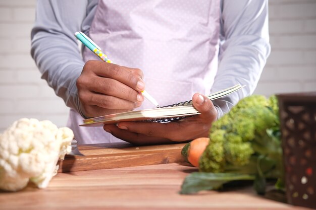 Joven escribiendo pan de dieta en el Bloc de notas en la mesa de la cocina