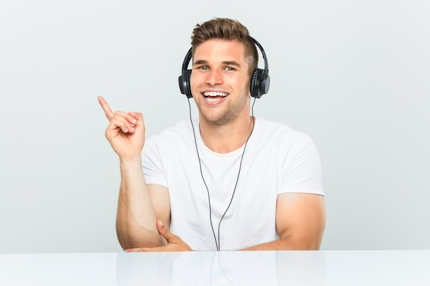 Joven escuchando música con auriculares sonriendo alegremente señalando con el dedo lejos.