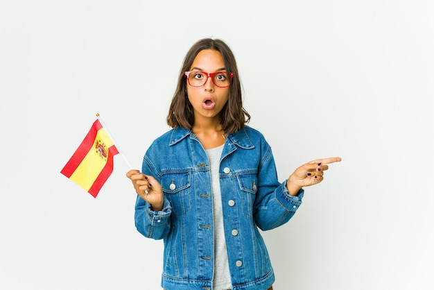 Joven española sosteniendo una bandera aislada en la pared blanca apuntando hacia el lado
