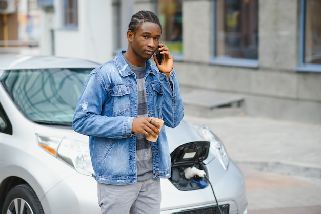 Joven esperando su coche eléctrico para ser cargado