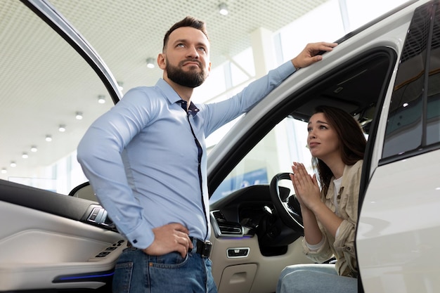 Foto una joven esposa convence a un hombre para que le compre un auto nuevo en un concesionario de autos.