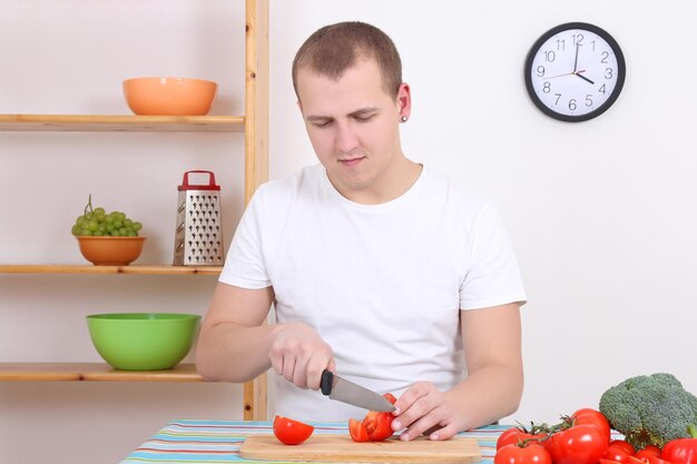 Joven esposo cortando tomate en la cocina