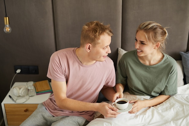 Joven esposo trayendo a su esposa una taza de café negro en la cama