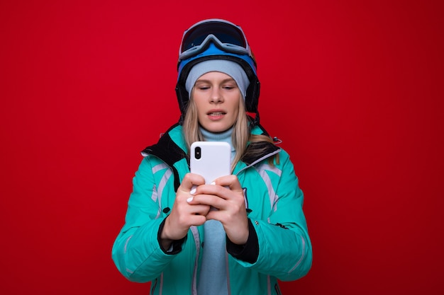 Una joven esquiador escribe en su teléfono sobre un fondo rojo.