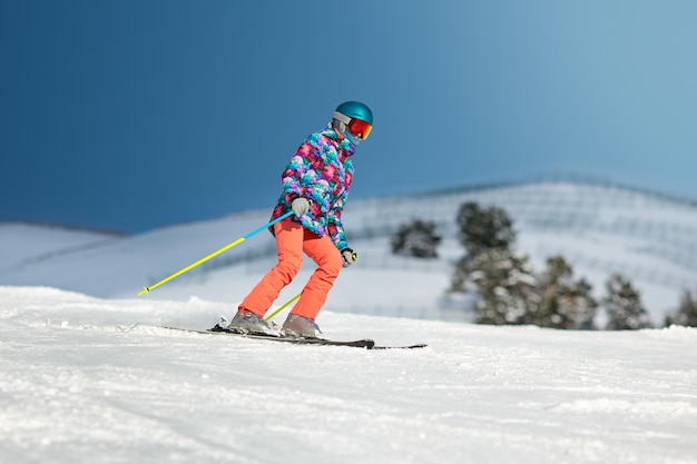 Joven esquiadora deslizándose por la pendiente en un día soleado en un resort de montaña