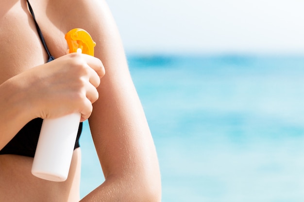 Joven está aplicando crema solar protectora sobre su hombro en la playa.