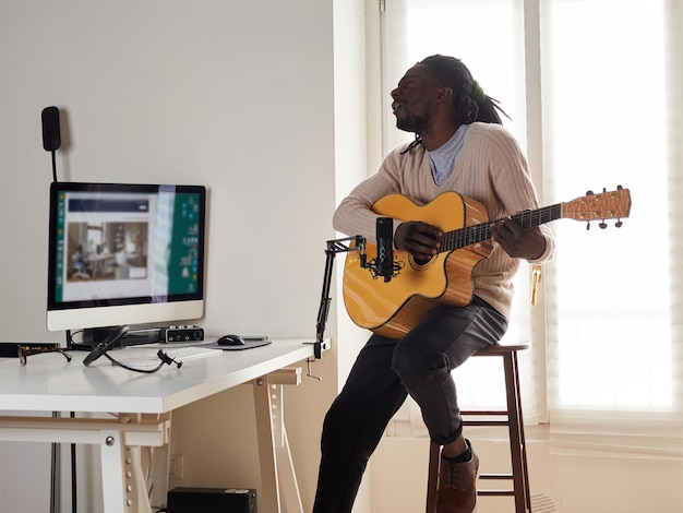 El joven está cantando y tocando la guitarra mientras hace una grabación de audio en casa