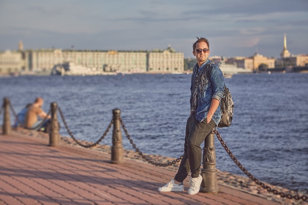 Joven está cruzando el paseo marítimo del río Neva con mochila en San Petersburgo, Rusia.