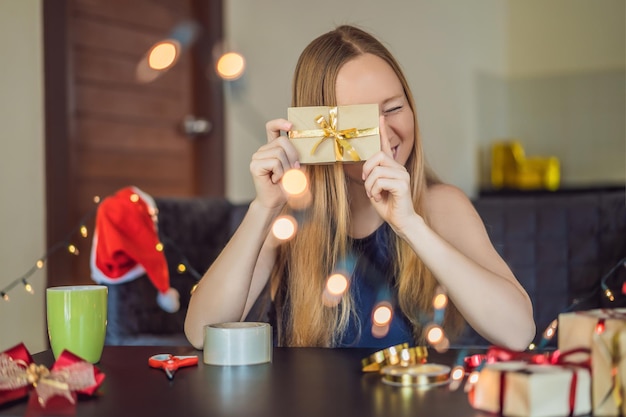 La joven está empacando regalos envueltos en papel artesanal con una cinta roja y dorada para