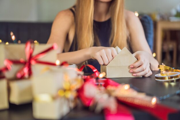 La joven está empacando regalos envueltos en papel artesanal con una cinta roja y dorada para