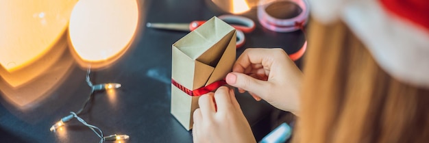 La joven está empacando regalos envueltos en papel artesanal con una cinta roja y dorada para