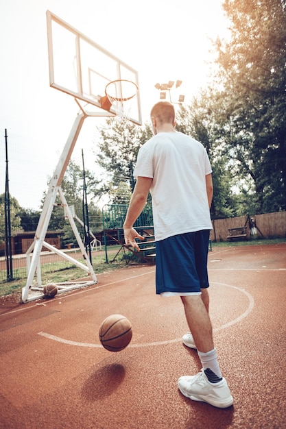 El joven está entrenando baloncesto en la cancha de la calle. Él está listo para tomar la pelota.