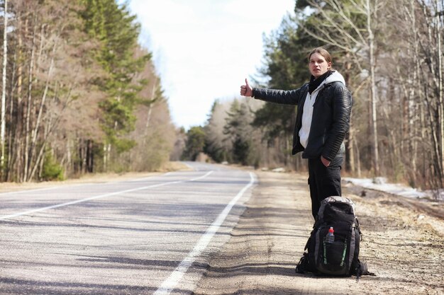 Un joven está haciendo autostop por todo el país El hombre está tratando de atrapar un automóvil que pasa para viajar El hombre con la mochila se fue haciendo autostop hacia el sur