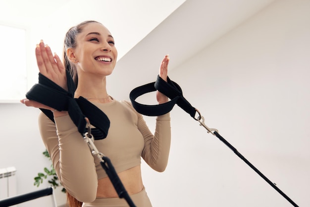 Una joven está haciendo pilates en una cama reformadora en un estudio luminoso, una hermosa morena esbelta en un