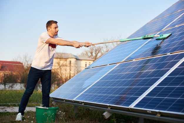 Un joven está limpiando un panel solar en una parcela cerca de la casa