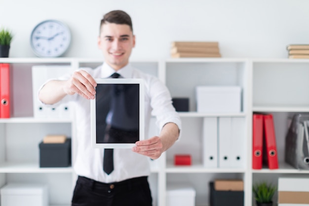 El joven está en la oficina y sosteniendo unas tabletas.