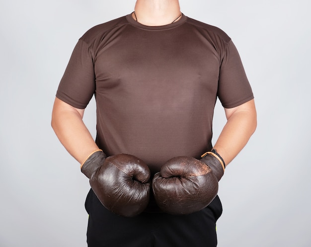 Joven está parado con guantes de boxeo marrón vintage muy viejos en sus manos